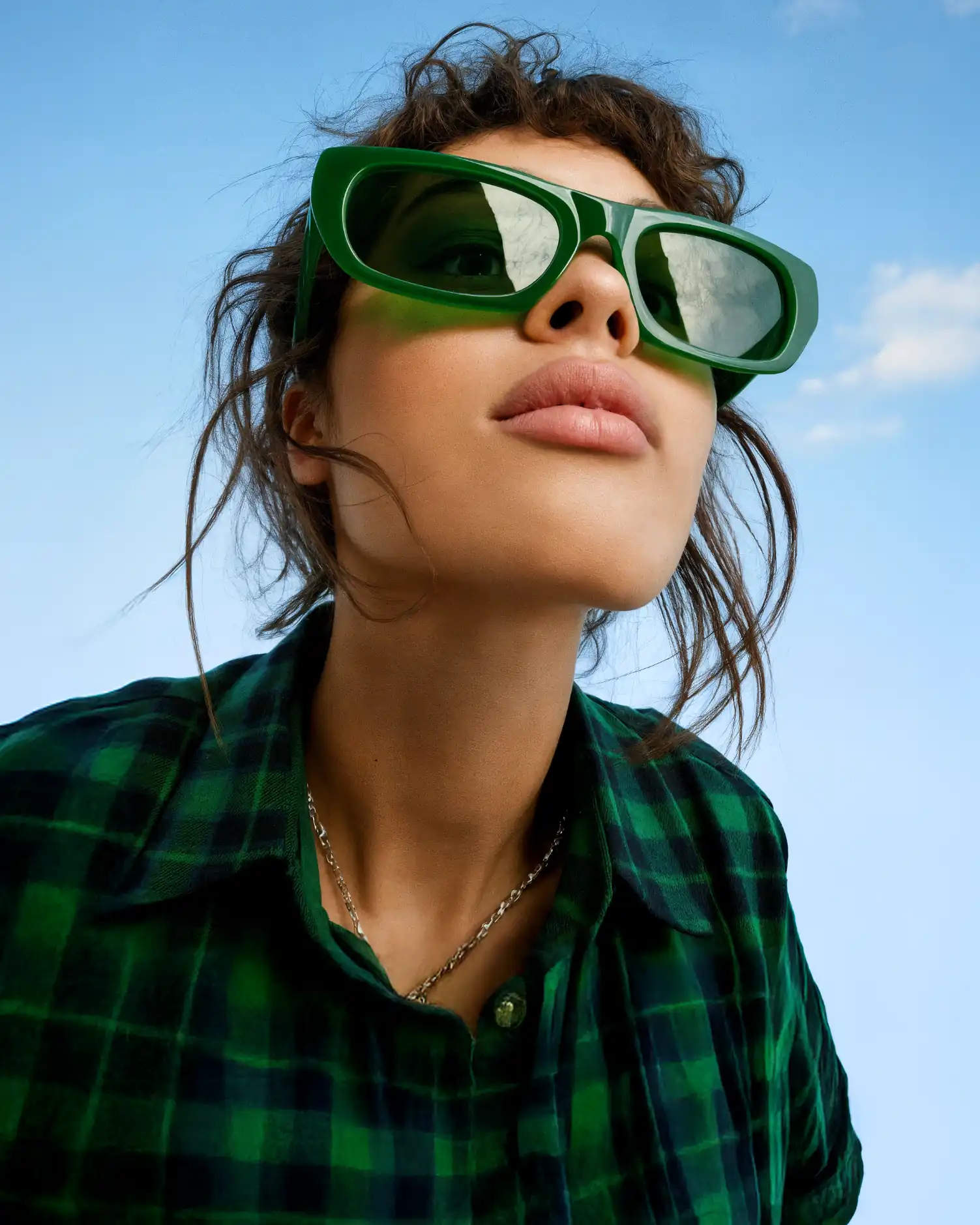 A person in green sunglasses looking up at a blue sky